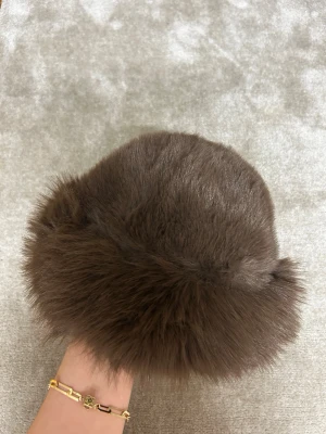 Brun fluffig pälsväst - Säljer en supermjuk och fluffig brun pälsväst med rundad form. Västen har en lyxig look och är tillverkad i pälsmaterial som ger en varm och cozy känsla. Perfekt för dig som vill sticka ut med en cool och trendig stil.