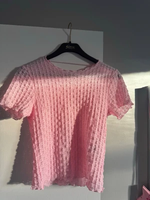 Rosa spetsblus från AWARE - Säljer en söt rosa blus från AWARE i storlek M. Blusen är gjord i spets med ett vågigt, ribbat mönster och har korta ärmar. Den har rund halsringning och transparent material som ger en lätt och luftig känsla. Perfekt för vår och sommar!