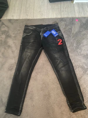 Svarta skinny jeans från Dsquared2 - Svarta jeans från Dsquared2 medd D2-tryck i rött och svart på framsidan. Jeansen har klassisk femficksdesign, svarta sömmar och lätt slitna detaljer för en edgy look. Materialet är jeans och de har midwaist.