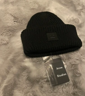 Svart mössa Acne Studios - Säljer denna snygga svarta mössan från Acne Studios med den klassiska ansiktsloggan framtill. Perfekt för kallare dagar :)