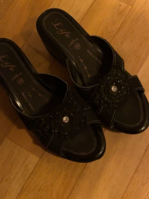 Svarta sandaler med blomdetalj - Säljer ett par svarta sandaler som är så extremt gulliga men för stora för mig, storlek 39🌷