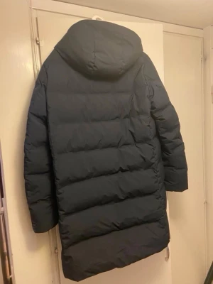 Svart lång pufferjacka med huva -  oanvänd uniqlo jacka i storlek S blå lång pufferjacka med huva och hög krage. Jackan har raka linjer, diskret dragkedja och är quiltad för extra värme. Perfekt för kalla dagar och har en clean look som funkar till de flesta stilar.