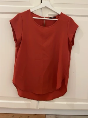 Röd blus från ONLY strl 36 - Säljer en röd blus från ONLY i storlek 36. Blusen har rund halsringning, korta ärmar och en snygg dragkedja i ryggen. Materialet är lätt och har en slät yta, perfekt för dig som gillar enkel och stilren design.