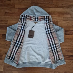Burberry Hoodie +tiger of sweden jeans på köpet! - Letar du efter en stilren och lyxig hoodie? Denna helt nya grå Burberry-hoodie kombinerar elegans med hög komfort. Den har Burberrys ikoniska rutmönster i fodret och en diskret logga på bröstet för en exklusiv touch. Tillverkad av mjukt, slitstarkt material och utrustad med dragkedja samt huva – både praktisk och stilfull. Perfekt för kalla dagar 🥶📌 Skick: Ny med taggar. 📦 Snabb leverans – skickas samma dag! 