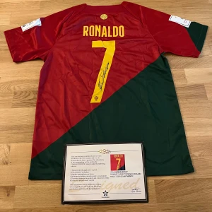 Portugal Ronaldo 7 signerad matchtröja - Portugal fotbollströja från Nike med Ronaldo 7 och stor gul signatur på ryggen. Tröjan har röd och grön diagonal design, gula detaljer och officiellt landslagsmärke på bröstet. Korta ärmar och tillverkad i lätt polyestermaterial. Certifikat för äkthet medföljer.