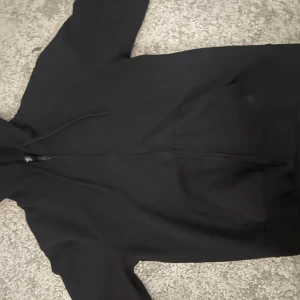 Svart hoodie med dragkedja från SOC - Svart hoodie från SOC i storlek S med hel dragkedja framtill och justerbar huva med snören. Perfekt basic-plagg med lång ärm och känguruficka, tillverkad i mjukt material som passar till chill eller träning. Har inte använd den någon gång vill att någon som verkligen vill använd köpa. Priset kan diskuteras 