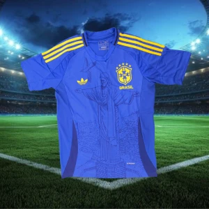 Blå Brasilien fotbollströja Adidas - Snygg blå Brasilien fotbollströja från Adidas med gula detaljer och tre ränder på axlarna. Tryck av Kristusstatyn på framsidan och Brasilien-emblem på bröstet. Perfekt för dig som vill sticka ut på planen eller läktaren.