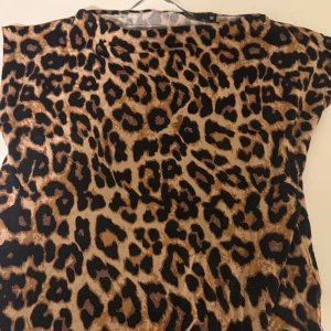 Leopardmönstrad topp från The Black Label - Säljer en snygg topp i leopardmönster från The Black Label Collection. Toppen har korta ärmar och är i mjukt, stretchigt material. Färgerna går i beige, brunt och svart, vilket ger en riktigt cool look. Perfekt för dig som vill sticka ut lite extra.