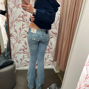 True Religion Jeans - Superpopulära ljusblå jeans från True Religion med klassiska kontrastsömmar och ikoniska fickdetaljer bak. Modellen Joey och har bootcut-ben och en så fin låg midja. Storlek W25 men passar xxs/xs/s. Lite slitna längst  ner på baksidan men är inget som man tänker på så de är i bra skick❤️Midjemåttet är 38 cm och innerbenslängen är 82 cm🫶🏻