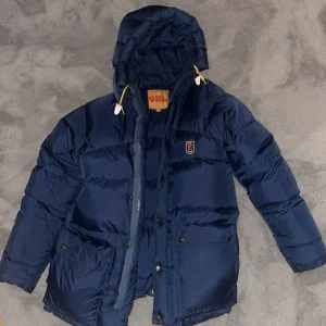 Fjällräven jacka - Marinblå fjällräven jacka i den äldre modellen  Expedition Down Jacket                                (tjockare än light versionen)                                               Jackan är tvättad 1 gång i tvättmaskin                                              Saknar undersidan av en knapp men inget som syns på eftersom ovansidan sitter kvar 🤗                 Skriv gärna vid frågor 🥰