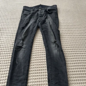 Svarta Dsquared2 jeans  - Snygga svarta jeans från Dsquared2 med slitna detaljer på benen. Jeansen har klassisk femficksdesign, diskreta färgstänk på baksidan och Dsquared2-logga på både läderpatch och ficka. Perfekt för dig som gillar en edgy streetstil.