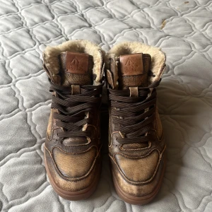 Bruna vinterskor från Ralph lauren med mjuk päls på insidan - Snygga bruna high-top vinterskor från Polo med mjukt fuskpälsfoder och skinnliknande yta. Skorna har bruna snören, rund tå och platt sula. Perfekta för kalla dagar med sin varma insida och fin vinterstil. Polo-logga på sidan och gummisula med bra grepp. Jag säljer dem eftersom de är för små för mig. Ny pristet för skorna är 1300 därför säljer jag dem för 600 jag och öppen för prisförslag.