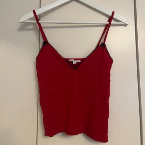 Röd topp med spets från Subdued - Söt topp med rosetter och spetsdetaljer. Använd ett fåtal gånger, mycket fint skick! Storlek m, men den är ganska liten i storleken och passar mer som xs/s. 