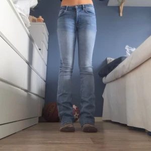 Bootcut jeans från Zara, ljusblå, strl 36 - Säljer ett par ljusblå bootcut jeans från Zara i storlek 36. De har klassisk femficksdesign, dragkedja och knapp framtill. Jeansen är midwaist och har en snygg tvättad look med lätt utsvängda ben. Har ett håll imellan benen 