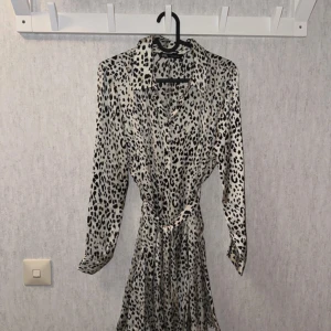 Leopardmönstrad miniklänning storlek s - Snygg kort leopardmönstrad klänning från Zara  i glansigt material. Klänningen har långa ärmar, knappar framtill, klassisk krage och knytskärp i midjan för en smickrande passform. Helt nytt