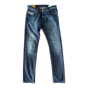 Diesel slim fit jeans blå - Snygga blå jeans från Diesel, modell Tepphar Slim. De har klassisk femficksdesign, kontrastsömmar och en slim passform. Jeansen är tillverkade i stretchigt denim för extra komfort och har en mörk tvätt med slitningar. Storlek W31 L32