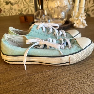 Converse All Star sneakers - Säljer ett par klassiska Converse All Star sneakers i mintgrönt tyg med vita gummitåhättor och vit sula med svart rand. Skorna har vit snörning och låg profil, perfekt för dig som gillar en chill och retro stil.