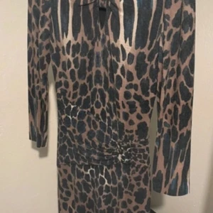 Leopardmönstrad klänning med knut - Snygg leopardmönstrad klänning med trekvartsärm och knutdetalj i midjan. Klänningen har en figurnära passform och är perfekt för dig som vill sticka ut med ett djurmönster. Färgerna går i beige och svart för en cool look.