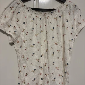 Vit blommig blus från 157 - Supersöt vit blus från 157 med små blommor i rosa, blått och grönt. Blusen har korta ärmar, rynkad resår vid halsen och en luftig, lätt struktur. Perfekt för en fräsch och somrig look! (Aldrig använt) priset kan även diskuteras 