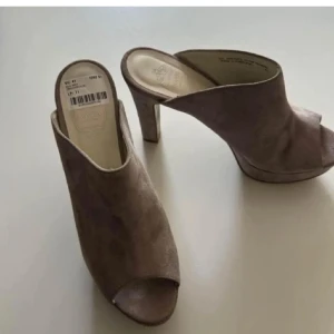 Skor i mocka  - Säljer ett par beige mules från Novita i mjuk mocka. Skorna har öppen tå, hög klack och en stilren design som passar perfekt till många outfits. Bekväma att bära och enkla att ta på tack vare slip-in modellen. Stl 41 men passade min fot som är 39 