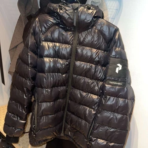 Svart Peak Performance Jacka  - Peak Performance vinterjacka till salu Snygg och varm jacka från Peak Performance. Håller bra mot kyla, vind och snö. Bekväm att ha på sig och i fint skick. Jackan har även huva med justerbart band och två sidofickor med dragkedja.