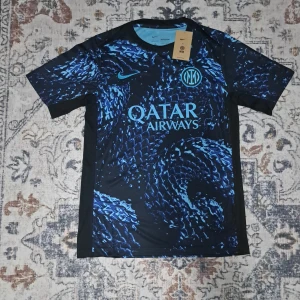 Inter Nike blå fotbollströja M - Säljer en officiell Inter fotbollströja från Nike i storlek M. Tröjan har ett unikt blått och svart mönster med klubbmärke och Qatar Airways-tryck på bröstet. Tillverkad i lätt och ventilerande material, perfekt för match eller träning.