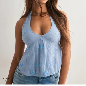 Ljusblå halterneck topp med paljetter - Säljer en ljusblå halterneck topp med v-ringning och öppen rygg. Toppen har snygga paljettdetaljer och knyt i ryggen för en justerbar passform. Perfekt för dig som vill sticka ut med en glittrig och trendig look. Passar till jeans eller kjol för en cool vibe. Helt oanvänd!