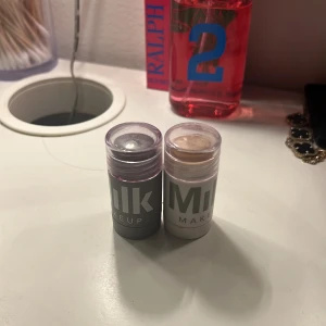 Milk Makeup highlighter och blush stick - Två smidiga stick från Milk Makeup – en highlighter i silver och en blush i varm mörkrosa ton. Perfekta att ta med i väskan och enkla att applicera direkt på huden. Kommer i praktiska plastförpackningar med skruvlock.