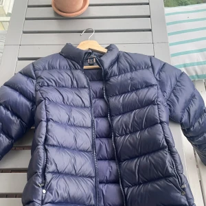 Mörkblå pufferjacka Polo Ralph Lauren  - Säljer en mörkblå pufferjacka från Polo Ralph Lauren i storlek XL barn vilken motsvarar 160-170cm. Jackan har horisontella quiltade sektioner, dragkedja framtill och klassisk broderad logga på bröstet. Perfekt för kalla  vinter dagar och har en clean, sportig look. Jackan har varit använd ett tag men är fortfarande redo för en ny äger Haru några funderingar ställ de!😁