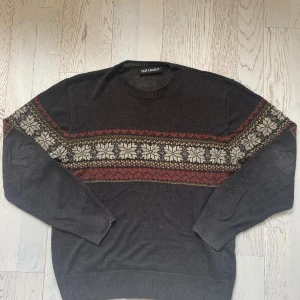 OUR LEGACY - Base Roundneck Mörkgrå mönstrad stickad tröja Our Legacy - Nypris 3600 Mörkgrå stickad tröja från Our Legacy med snyggt mönster i vitt, rött och beige över bröstet och ärmarna. Rund hals och ribbade muddar. Perfekt för dig som gillar retrovibbar och vill ha något unikt i garderoben.