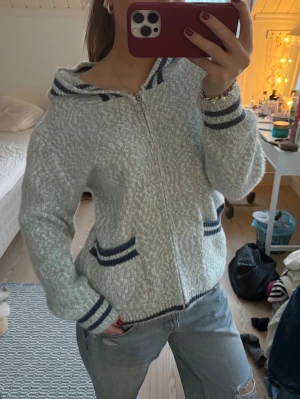 Ljusblå stickad hoodie med dragkedja - Står storlek M/L men passar mig perfekt som är storlek S som också gillar lite overzised. Annars mysig ljusblå stickad hoodie med dragkedja och huva. Tröjan har mörkblå ränder på muddar, fickor och huva samt två fickor framtill. Perfekt för kyliga dagar och har en relaxed, loose passform. 
