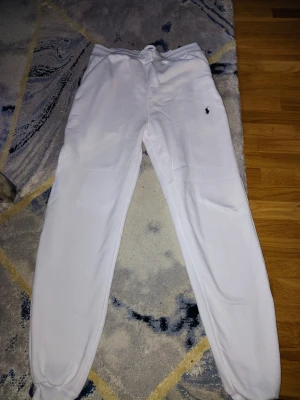 Vita mjukisbyxor Polo Ralph Lauren - Säljer ett par vita mjukisbyxor från Polo Ralph Lauren med klassisk logga broderad på benet. Byxorna har resår i midjan med snörning och muddar vid bensluten. Tillverkade i mjukt bomullsmaterial för maximal komfort.