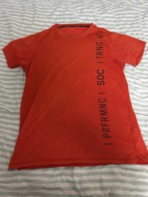 Orange tränings-tshirt från SOC - Snygg orange t-shirt från SOC med svart textprint längs framsidan. Klassisk rund halsringning och korta ärmar. Perfekt för träning och sportiga dagar. Tillverkad i ett lätt och bekvämt material som andas.