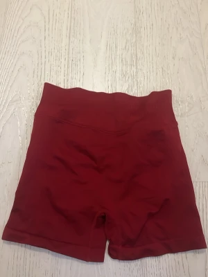 Röda seamless träningsshorts - Säljer ett par röda seamless shorts med hög midja och scrunch-detalj bak. Tillverkade i stretchigt material med 90% polyester och 10% elastan, perfekta för gymmet eller annan träning. Sitter tight och formar sig efter kroppen.