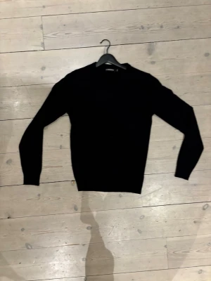Svart stickad tröja från J.Lindeberg merinoull - Klassisk svart stickad tröja från J.Lindeberg i storlek S. Tröjan har rund halsringning och långa ärmar, perfekt för lager på lager under kyliga dagar. Enkel och stilren design som funkar till det mesta. I merinoull 