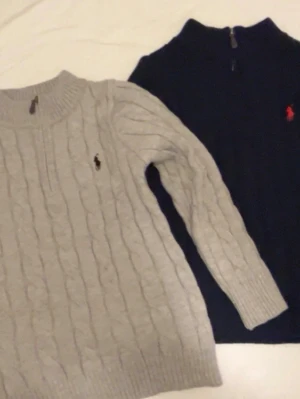 Marinblå/Grå kabelstickad tröja Polo Ralph Lauren - Kabelstickad marinblå/Grå tröja från Polo Ralph Lauren med halv dragkedja och klassisk röd/Svarta logga på bröstet. Tröjan har ribbade muddar och hög krage, perfekt för kyliga dagar.       Man kan köpa dom separat också då är det 600kr styck. Helt ny aldrig använda.