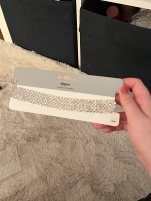 Glittrig silver choker från Appear - Säljer en bred, glittrig choker i silver från Appear. Halsbandet har flera rader med gnistrande stenar och justerbart spänne i bak. Perfekt accessoar för att lyfta din outfit med extra bling.