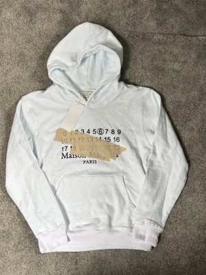 Vit maison margiella hoddie - Säljer nu denna snygga hoddie, -jättefint skick (ny med tags) -storlek M -ser nästan ljusblå ut på bilden men den e vit✅ (Hör gärna av er vid frågor )🙌🏼