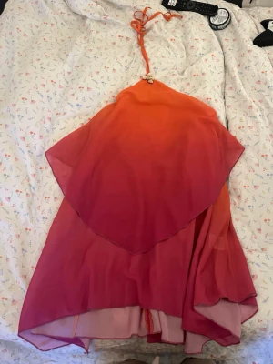 Ombre kortklänning från Peppermayo - Säljer en superfin ombre kortklänning från Peppermayo i orange och rosa toner. Klänningen har halterneck med snörning och volangdetaljer framtill. Perfekt för sommaren och ger riktiga strandvibbar.