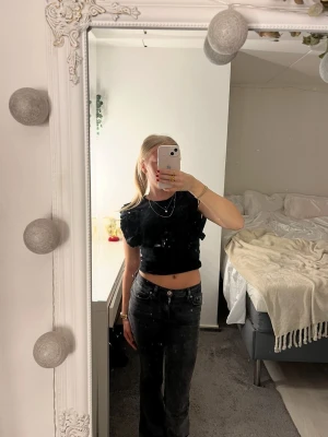 Svart croppad topp från Zara - Säljer en svart croppad topp från Zara med volangdetaljer på axlarna. Toppen är ärmlös och har en tight passform som framhäver midjan. Perfekt att styla med höga jeans eller kjol för en trendig look.