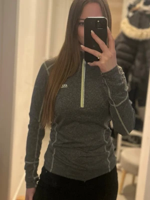  långärmad träningströja  -  grå långärmad träningströja från OTP  med ljusgröna detaljer och half zip framtill. Tröjan har en slim passform och är perfekt för träning eller utomhusaktiviteter. Snygga sömmar längs ärmar och sidor ger en sportig look.