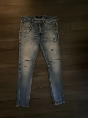 Replay  jeans med fabrikslitningar  - Säljer ett par blåa Replay jeans med slitningar  på benen. Perfekta för dig som gillar en avslappnad men trendig look. Inga defekter eller likande, som nya!Priset är diskuterbart via snabb affär. Inga defekter eller likande. W32 L34