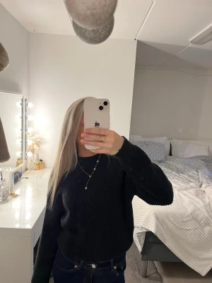 Svart stickad tröja med rund hals - Mysig svart stickad tröja med rund hals och långa ärmar. Tröjan har en enkel, ribbad struktur och en relaxed passform som är perfekt för kyligare dagar. Passar till både jeans och kjol för en clean look.