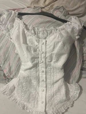 Vit spetsblus från SHEIN - Supersöt vit blus från SHEIN i storlek S. Blusen har broderade blommor, volangkant, pärlknappar framtill och romantiska detaljer. Materialet är lätt och luftigt med spets och broderier, perfekt för sommarens alla tillfällen.