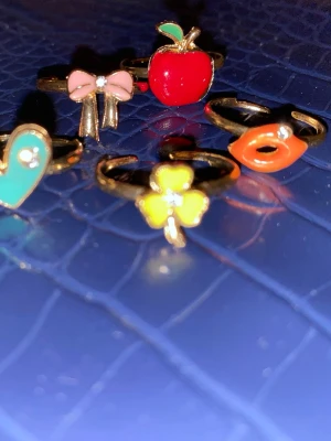 Justerbara ringar - Bilden visar flera färgglada ringar med olika motiv som rosett, äpple, läppar, hjärta och blomma. 