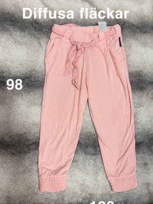 Ljusrosa byxor med knytband, strl 98 - Säljer ett par ljusrosa byxor med knytband i midjan och resår vid bensluten. Byxorna har en avslappnad passform. Perfekta för en chill och bekväm stil.🌸 Diffusa fläckar. Storlek 98