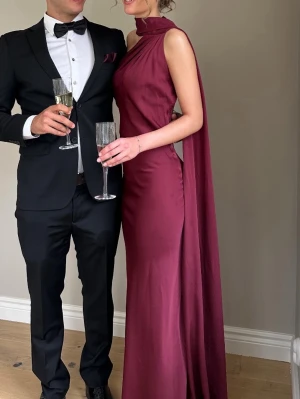 Vinröd långklänning med cape - Säljer min vinröda balklänning från Kaoâ som är använd 1 gång. Nypris är ca 3450kr. Klänningen är detaljerad och öppen i ryggen med guld knappar vid baksidan av nacken. Klänningen har även en lång cape som går hela vägen ner till marken. Jag är 174cm lång. Skriv vid intresse så skickar jag bild på defekter.😊