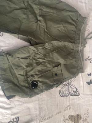 Gröna shorts från C.P. Company - Snygga gröna shorts från C.P. Company med elastisk midja och snörning. Shortsen har en ikonisk linsdetalj på benfickan och är tillverkade i ett lätt och svalt material, perfekt för varma dagar. Stilsäkra och bekväma med meshfoder på insidan. Nytt och oanvänd. pris kan diskuteras.