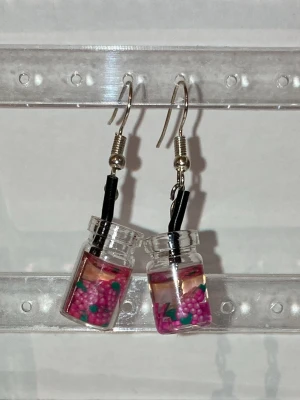 Örhängen  -  Handgjorda örhängen som görs av mig. Med rosa frukter i ett glas. Frakten är ca 22-100kr beroende på vikten på produkten . Kontakta mig om du vill köpa.