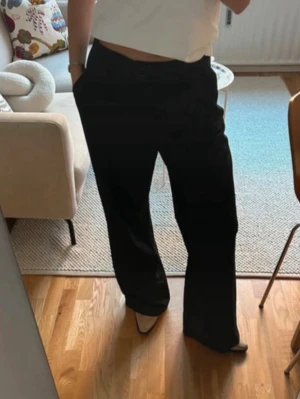 Svarta kostymbyxor från Zara - Säljer ett par svarta kostymbyxor från Zara med klassisk rak passform och vida ben. Byxorna har hällor för bälte och stängs med dragkedja och knapp. Perfekta till en stilren look och tillverkade i ett mjukt material som känns bekvämt hela dagen.